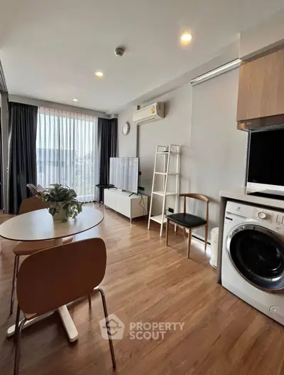 Modern living room with wooden flooring, dining area, and in-unit washing machine.