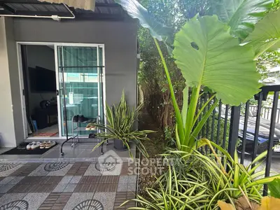 Charming outdoor patio with lush greenery and modern sliding glass door entrance.