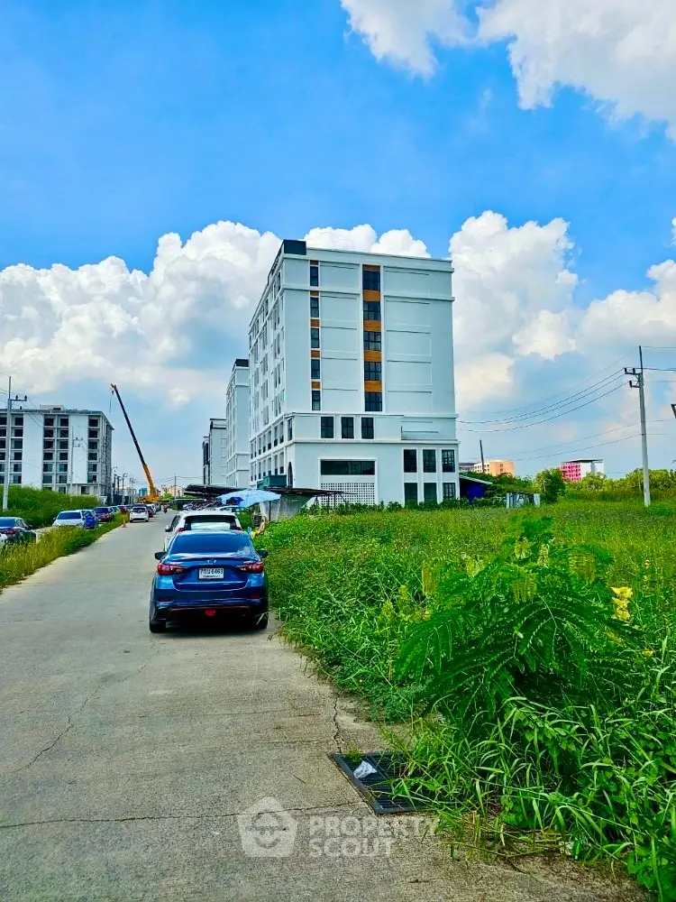 Modern multi-story residential building with ample parking, set against a blue sky with lush greenery in the foreground, offering a blend of urban living and nature.