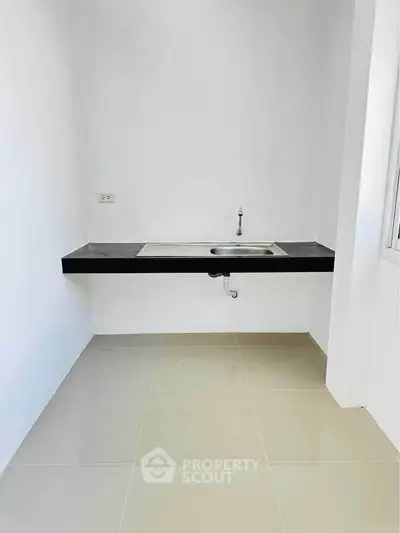 Minimalist kitchen area with sleek black countertop and modern sink design.