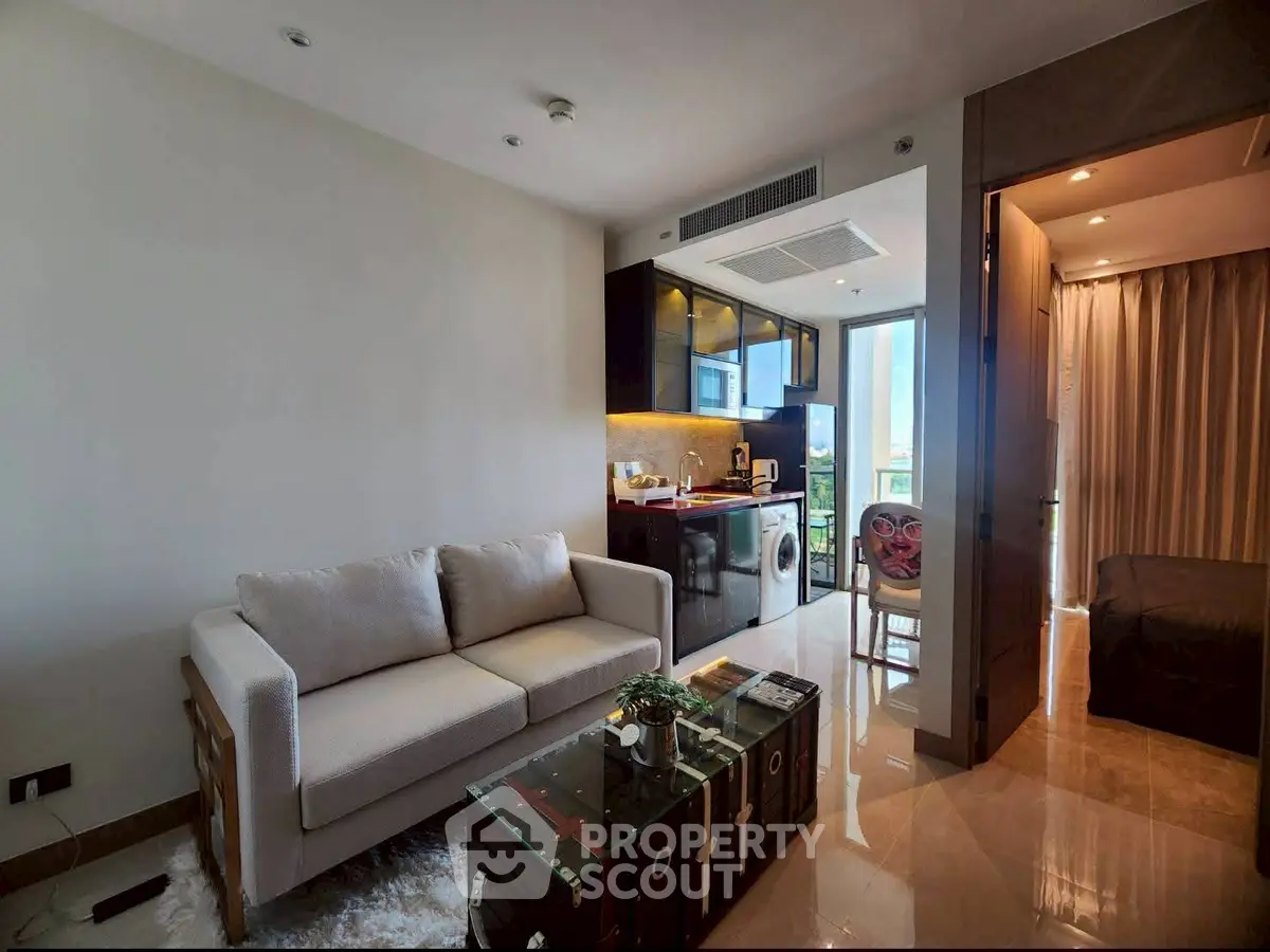 Modern living room with open kitchen and washing machine, featuring elegant decor and natural light.