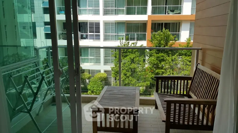 Charming balcony with wooden furniture and lush garden view in modern apartment complex.