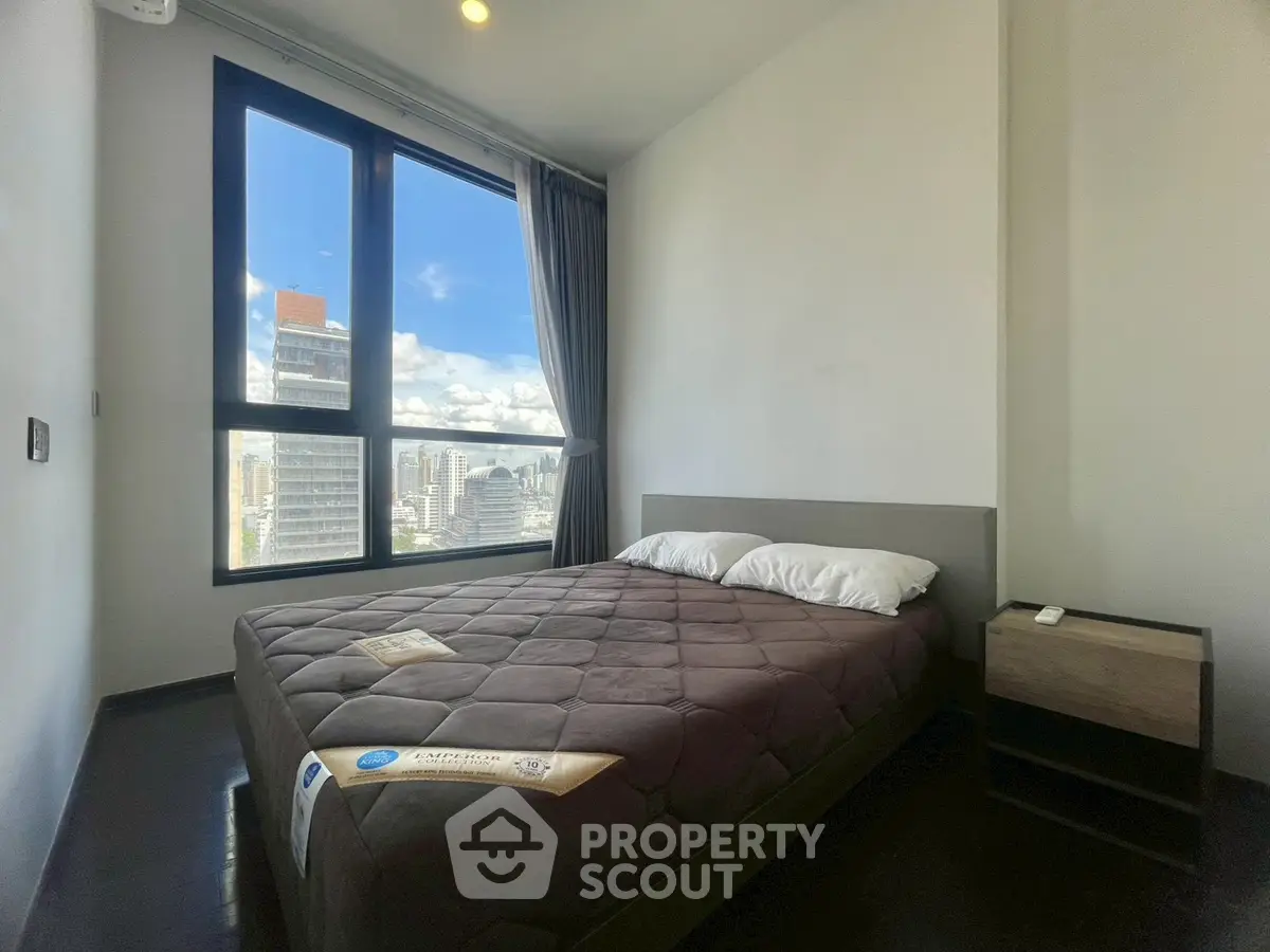 Modern bedroom with city view, featuring a cozy bed and large window for natural light.