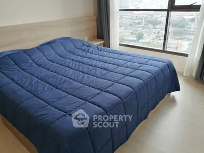 Spacious bedroom with large window offering stunning city views, featuring a cozy blue comforter on a wooden bed.