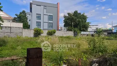 Vacant land with lush greenery and modern building backdrop, perfect for development opportunities.