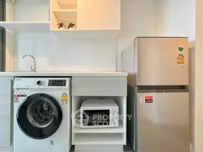 Modern kitchen with washing machine, microwave, and fridge in sleek design.
