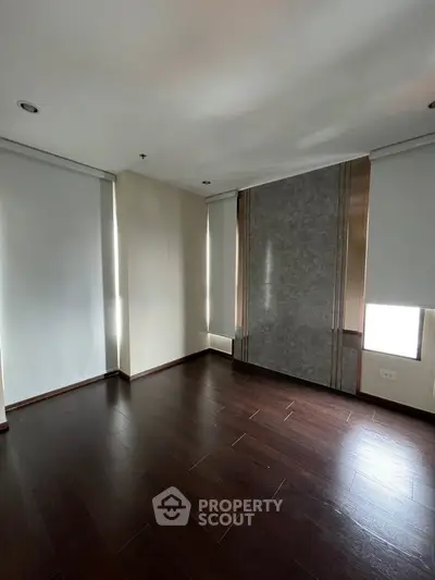 Spacious empty room with dark wood flooring and modern window shades.