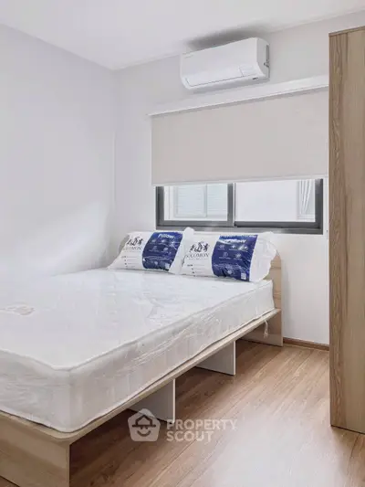 Modern bedroom with minimalist design, featuring a comfortable bed, wooden flooring, and air conditioning.