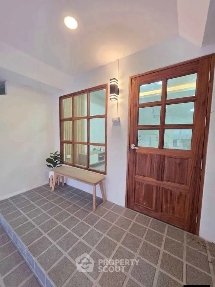 Charming entrance with wooden door and window, featuring a cozy bench and stylish lighting.