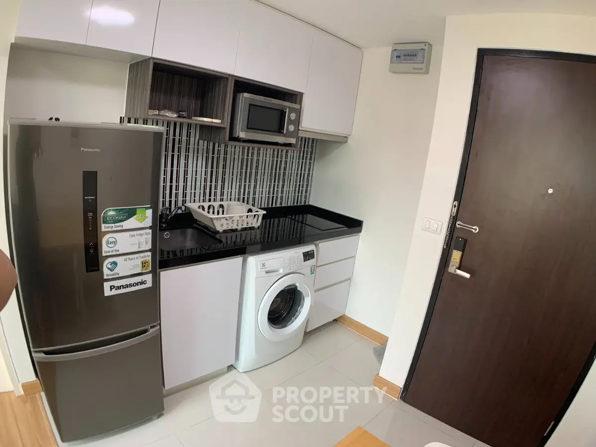 Modern compact kitchen with sleek appliances and washing machine in stylish apartment.