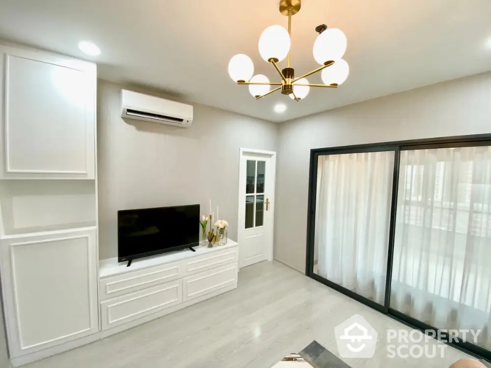 Elegant living room with modern gold chandelier, sleek white built-in cabinets, and large sliding glass doors leading to a bright, airy balcony.