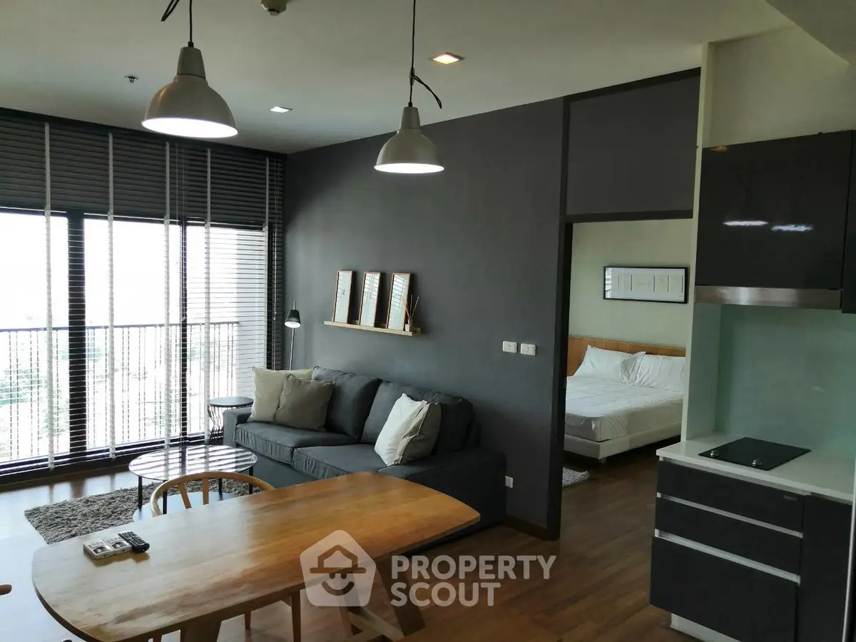 Modern open-plan living room with dining area and bedroom view, featuring sleek furniture and large windows.
