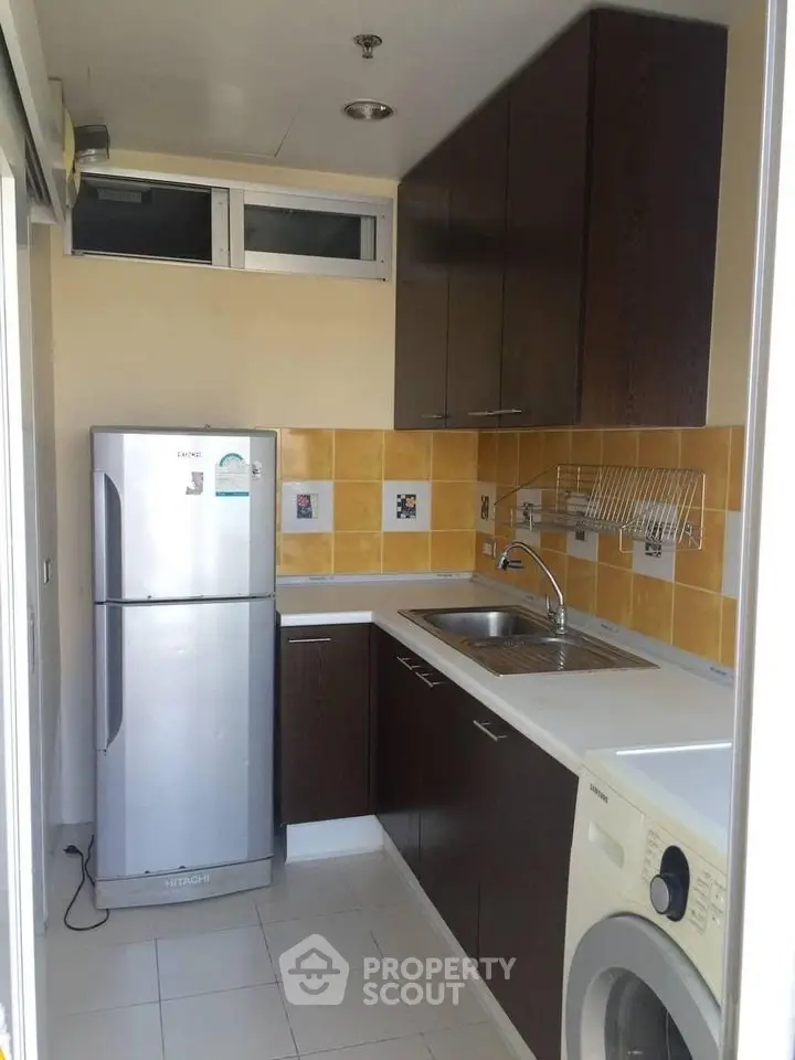 Modern kitchen with sleek cabinets, stainless steel fridge, and washing machine in compact layout.