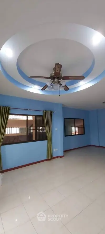 Spacious living room with modern ceiling fan and large windows in a bright blue interior.