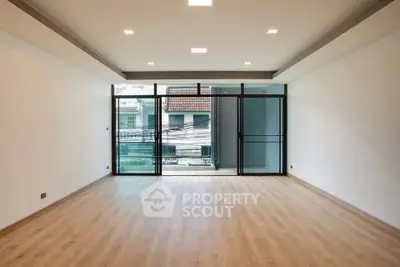 Spacious modern living room with large windows and wooden flooring, offering ample natural light and a serene view.