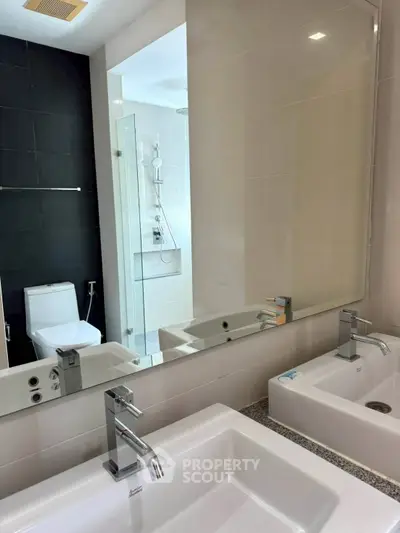 Modern bathroom with dual sinks and glass shower enclosure in sleek design.