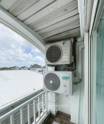 Balcony with air conditioning units and a view of rooftops and sky.