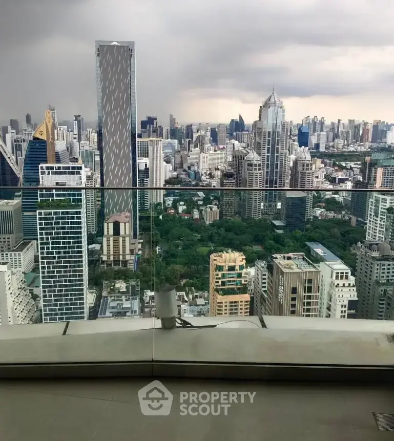 Stunning cityscape view from a high-rise balcony with glass railing, showcasing urban skyline and greenery.