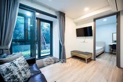 Modern living room with large windows and garden view, connected to a cozy bedroom.