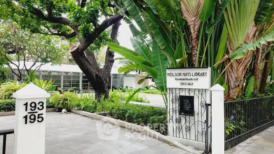 Charming library entrance surrounded by lush greenery and tropical plants, offering a serene reading environment.