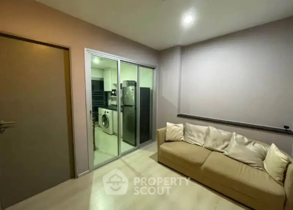 Modern living room with beige sofa and glass doors leading to a laundry area with washing machine.
