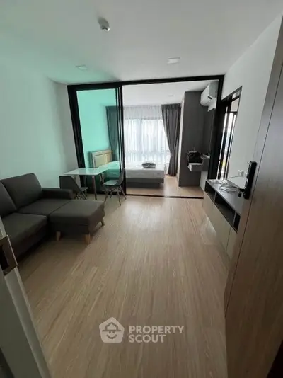 Modern studio apartment with open layout, featuring a cozy living area and bedroom separated by glass doors.