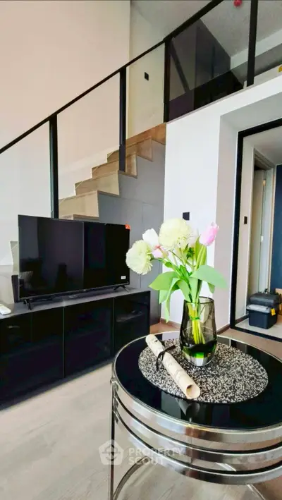 Modern living room with stylish decor and staircase, featuring a sleek TV setup and elegant floral arrangement.