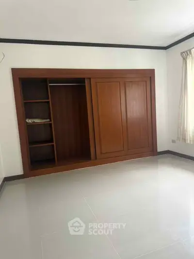 Spacious bedroom with built-in wooden wardrobe and tiled flooring, perfect for modern living.