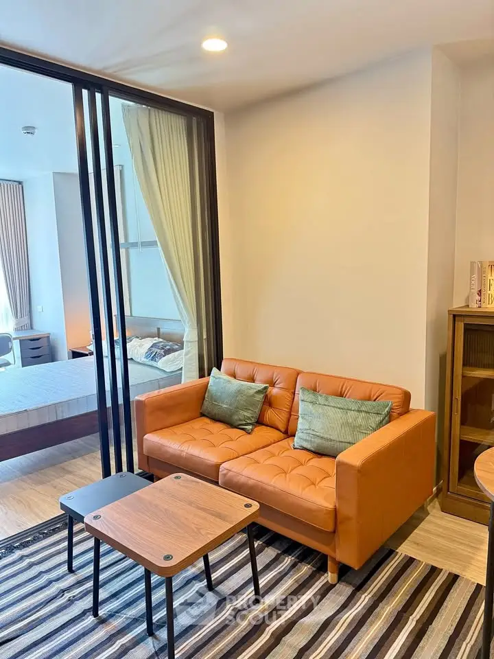 Modern living room with stylish orange sofa and glass partition leading to cozy bedroom.