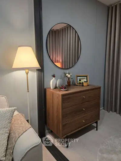 Stylish living room corner with elegant lamp, round mirror, and chic wooden dresser.