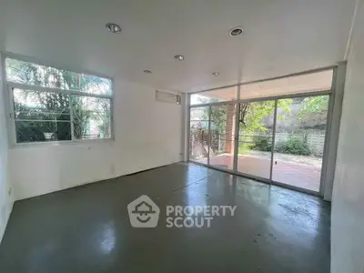 Spacious empty room with large windows and sliding glass doors opening to a patio with greenery.