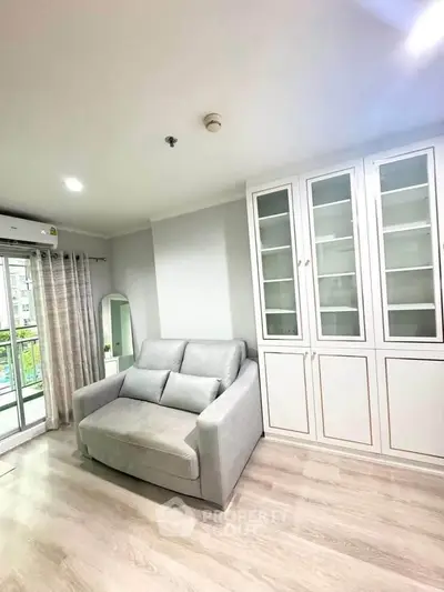 Modern living room with cozy sofa and elegant glass cabinet, featuring bright natural light and stylish decor.