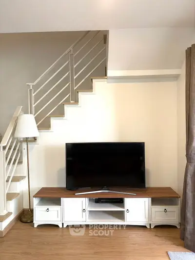 Charming living room with modern TV setup and elegant staircase, perfect for cozy family gatherings.