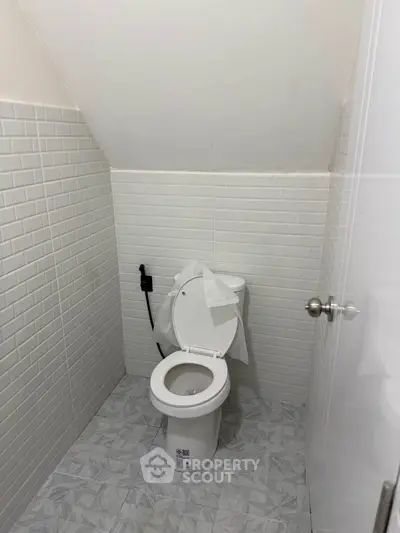 Compact bathroom with white tiled walls and modern toilet under sloped ceiling.