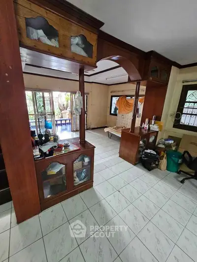 Spacious living room with wooden accents and tiled flooring, featuring large windows for natural light.
