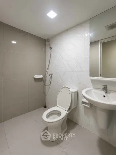 Modern bathroom with sleek fixtures and neutral tiles, featuring a shower and toilet.