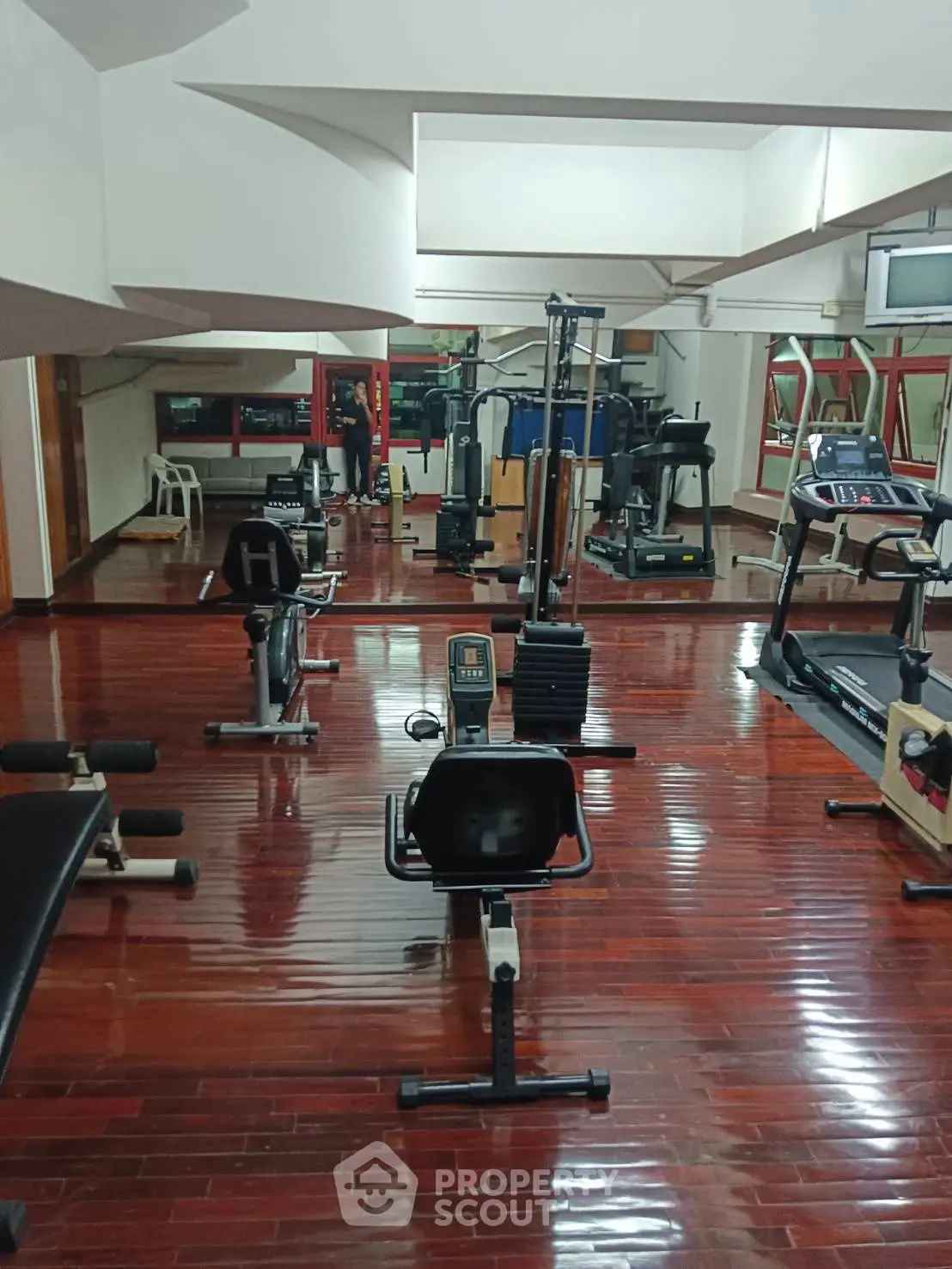 Spacious gym with modern equipment and polished wooden floors in a residential building.