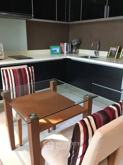 Modern kitchen with sleek black cabinets and glass dining table in a cozy apartment.