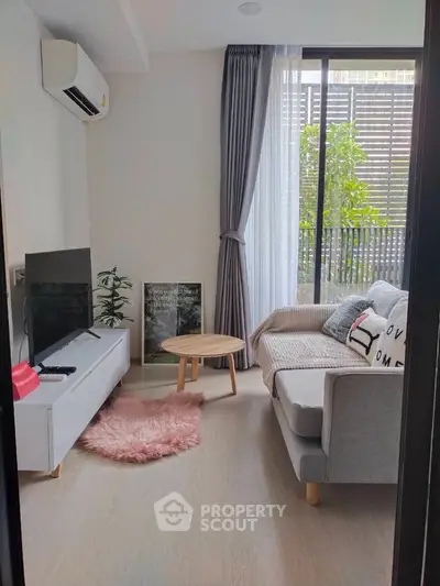 Cozy and modern living room with natural light, plush sofa, and sleek entertainment unit, leading to a serene balcony with greenery.