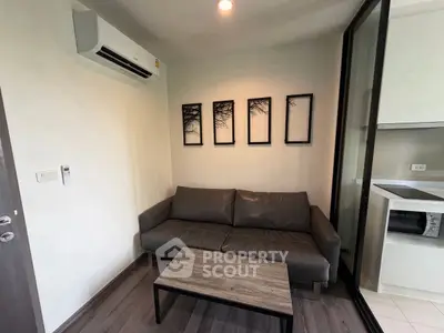 Modern living room with sleek sofa and wall art, adjacent to a compact kitchen area.