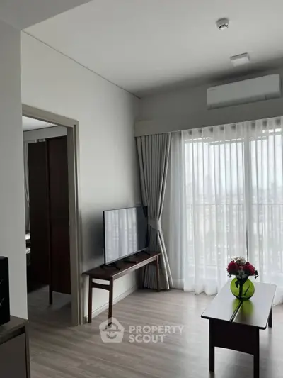 Modern living room with natural light, sleek furniture, and a view through sheer curtains.