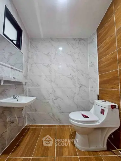 Modern bathroom with marble tiles and wooden accents, featuring a sleek toilet and sink.