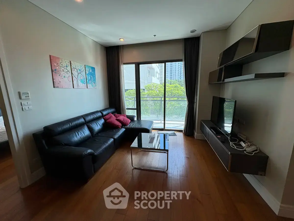 Modern living room with sleek black sofa, wall-mounted TV, and large window with city view.