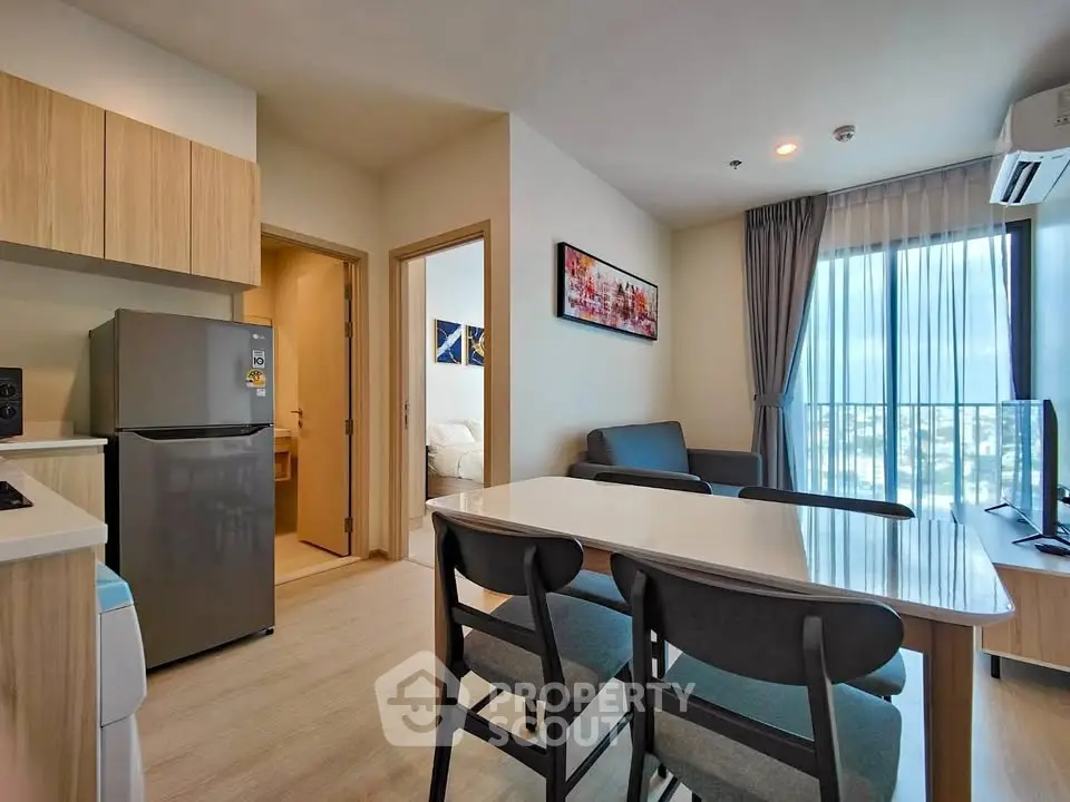 Modern open-plan living room with dining area and kitchen, featuring natural light and contemporary furnishings.
