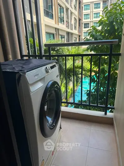 Charming balcony with washing machine overlooking lush greenery and pool in modern apartment complex.
