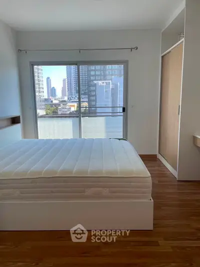 Modern bedroom with city view, featuring a large window and sleek wooden flooring.