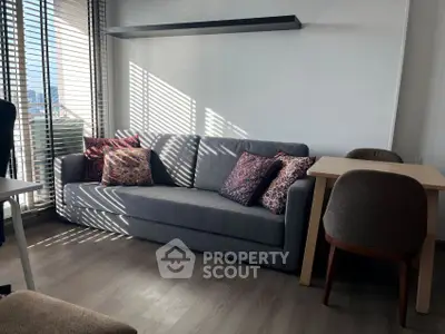 Modern living room with stylish gray sofa and dining area, featuring natural light and wooden flooring.