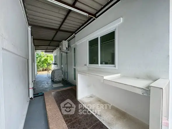 Spacious outdoor corridor with tiled flooring and window view, perfect for utility or storage use.