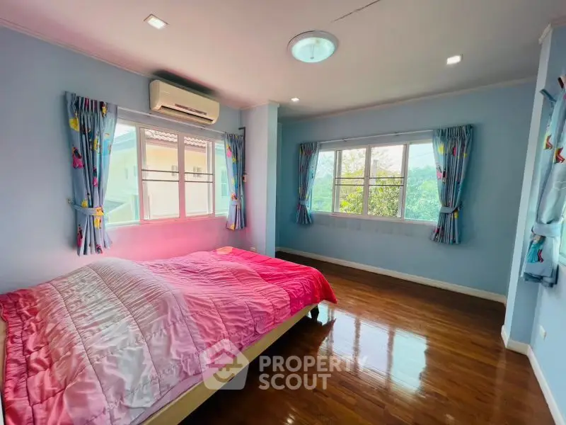 Spacious bedroom with large windows and wooden flooring in a cozy home.