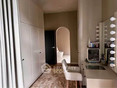 Elegant bedroom with vanity and walk-in closet, featuring a cozy chair and ample storage.